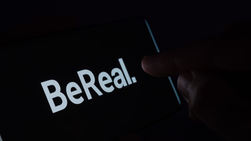 "暗いスマホ画面に表示されたBeRealロゴと、職場SNS投稿による情報漏洩リスクのイメージ"