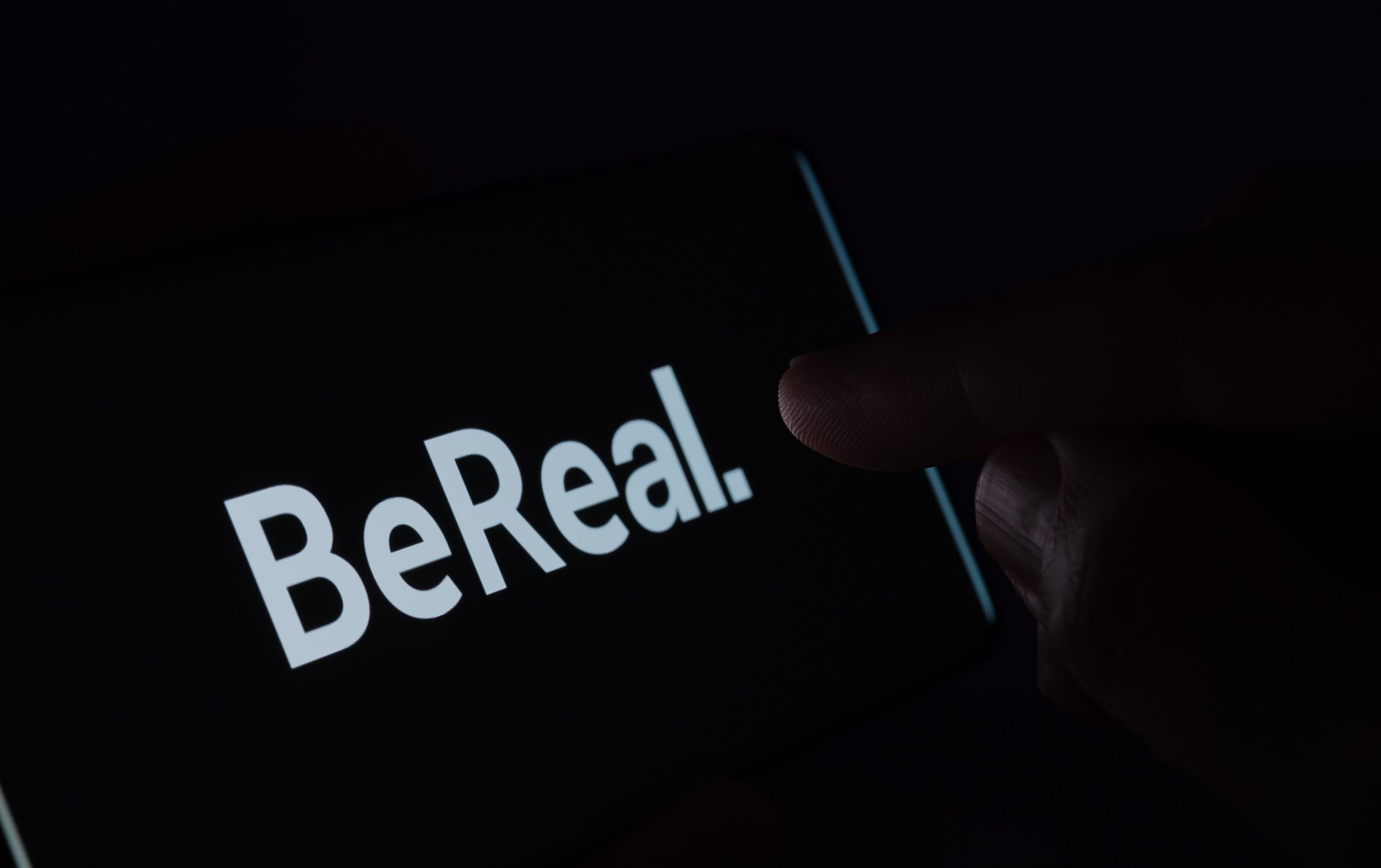"暗いスマホ画面に表示されたBeRealロゴと、職場SNS投稿による情報漏洩リスクのイメージ"